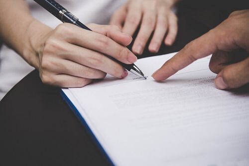 Close up of one hand holding a pen while another hand points at a marital agreement.
